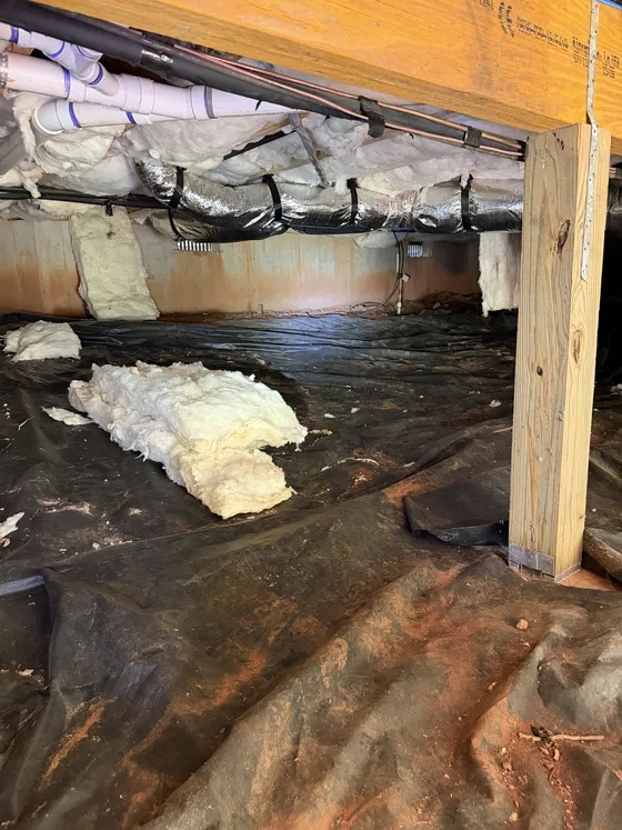 Crawl space before: fallen insulation on torn black plastic and red clay